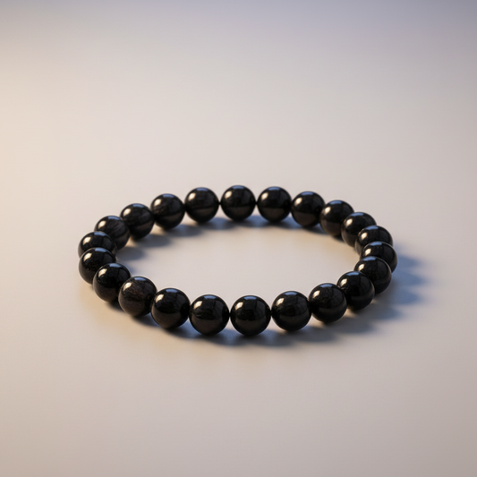 Black tourmaline round bead bracelet with deep polished black beads on soft gray surface with warm studio lighting